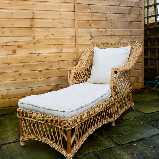 A vintage wicker day bed or chaise longue,with cream upholstered mattress and cushions